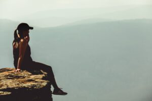 A woman sitting on a cliff overlooking the ocean, enjoying a peaceful and scenic view.