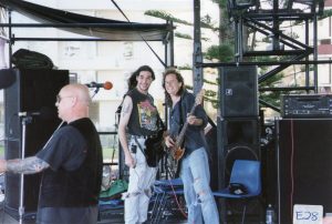 Nikk and Paul performing live with Angry Anderson on Manly Beach in 1998, showcasing a music event.